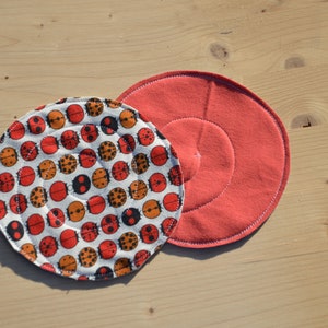 Puede incluir: Dos posavasos redondos de tela. Un posavasos es rojo y el otro tiene un fondo blanco con un patrón de mariquitas rojas y negras.