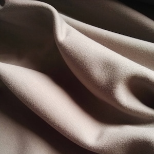May include: Close-up of a soft, beige fabric with a smooth texture and subtle wrinkles. The fabric is draped and folded, creating a gentle, flowing effect.