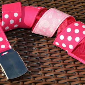 Könnte beinhalten: Ein pinkfarbener Gürtel mit weißen Punkten und einer silbernen Schnalle. Der Gürtel ist aus Stoff und hat ein gewebtes Design.