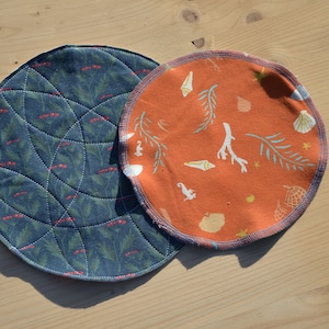 May include: Two round fabric coasters. One is blue with a geometric pattern and the other is orange with a seashell and seaweed design.