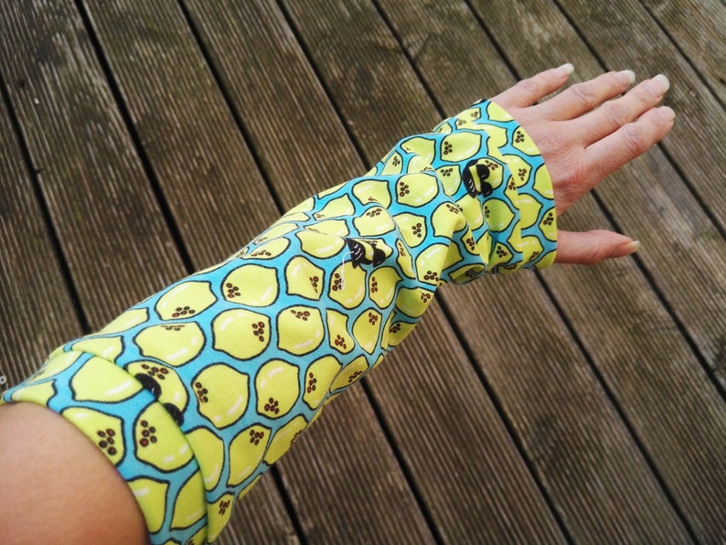 Pu&ograve; includere: Una manica in tessuto con un motivo a limoni. La manica &egrave; gialla con uno sfondo azzurro chiaro e un motivo ripetuto di limoni. La manica &egrave; indossata sul braccio.