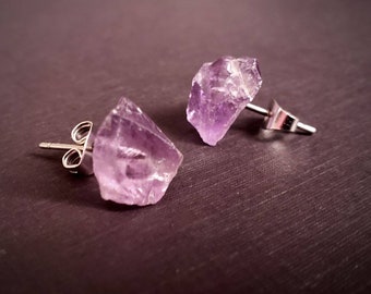 May include: A pair of amethyst crystal earrings with silver posts. The crystals are raw and have a natural, irregular shape.