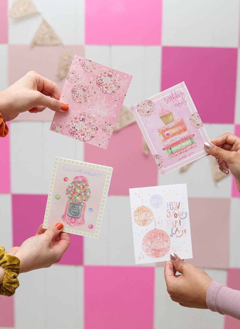 May include: Four pink and white greeting cards with different designs. The cards feature illustrations of disco balls, a gumball machine, a cupcake on a stack of books, and a disco ball with the text "Have a groovy birthday!"