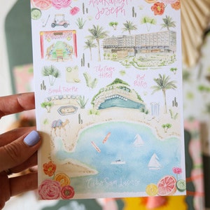 May include: A watercolor illustration of a wedding invitation with a map of Cabo San Lucas, Mexico. The map features a hotel, a pool party, a beach fire pit, and a golf cart. The text "Ana Karen + Joseph" is written at the top of the map.