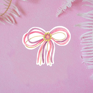May include: A watercolor illustration of a pink and purple bow with gold accents and a green and pink beaded center.
