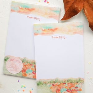 May include: Two memo pads featuring a watercolour design of a pumpkin patch. The top of each pad has a watercolour design of a sunset with stars. The text "Memo Patch" is printed on each pad.