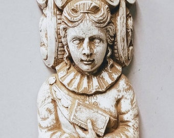 May include: A white plaster sculpture of a woman with a crown of leaves and flowers. She is holding a book in her hands and is wearing a long, flowing robe.