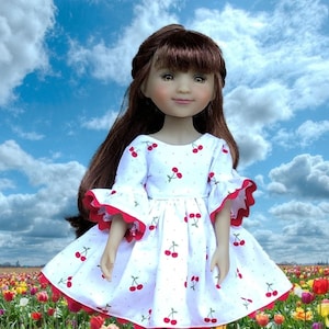 May include: A doll wearing a white dress with red cherries printed on it. The dress has red ruffled sleeves and a scalloped hem. The doll has brown hair and is standing in a field of colorful tulips.