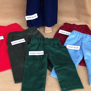 May include: A collection of colorful corduroy pants in various shades, including bright red, army green, dark green, dark red, light blue, and dark blue. Each pair has an elastic waistband and a label indicating the color.