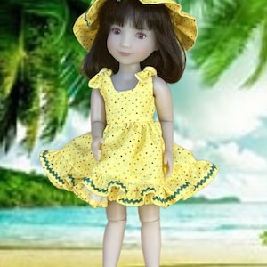 May include: A doll wearing a yellow polka dot dress and matching sun hat. The dress has a ruffled hem with green trim. The doll has dark hair and is posed against a tropical beach background.
