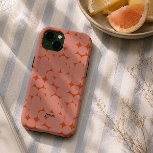 Op de afbeelding: Een koraalkleurig smartphonehoesje met een herhalend patroon van lichtroze afgeronde geometrische vormen en lijnen. Het woord pomni staat onderaan in het zwart gedrukt. Het hoesje heeft een donkergroene uitsparing voor de cameralenzen.