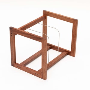 May include: A wooden wine rack with a rectangular frame design. The rack is made of dark brown wood and features thin, curved metal supports to hold bottles. The construction includes visible screws and small wooden pegs.