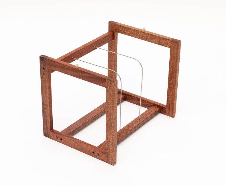 May include: A wooden wine rack with a rectangular frame design. The rack is made of dark brown wood and features thin, curved metal supports to hold bottles. The construction includes visible screws and small wooden pegs.