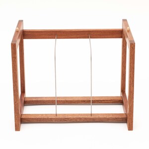 May include: A wooden wine rack with a rectangular frame and two vertical metal supports. The rack is made of reddish-brown wood and has a simple, minimalist design. The rack is designed to hold wine bottles.