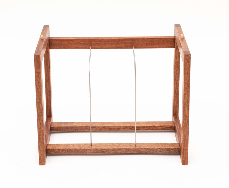 May include: A wooden wine rack with a rectangular frame and two vertical metal supports. The rack is made of reddish-brown wood and has a simple, minimalist design. The rack is designed to hold wine bottles.