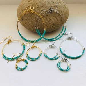 May include: Set of four turquoise beaded hoop earrings. The earrings are made with gold and silver wire and feature two rows of turquoise beads.