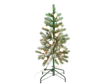 Op de afbeelding: Een kleine, kunstmatige kerstboom met groene takken bestrooid met witte vlokken. De boom is versierd met ronde, warmwitte lampjes en staat op een groene metalen standaard. Een wit netsnoer loopt vanaf de basis.