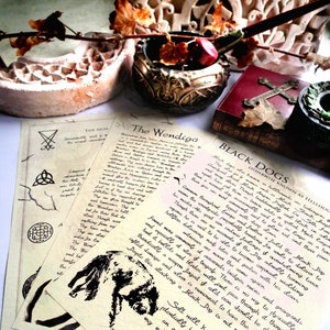 Puede incluir: Dos pergaminos de estilo vintage con texto escrito a mano sobre el Wendigo y los Perros Negros. Los pergaminos están sobre una superficie blanca con un tintero negro, una pluma y un libro rojo con una cruz.