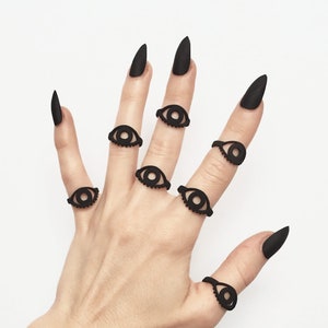 Multiple matte black 3d printed eye rings displayed on a gothic model hand with long black nails