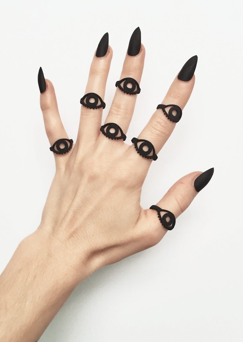 Multiple matte black 3d printed eye rings displayed on a gothic model hand with long black nails