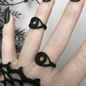 Matte black 3d printed eye ring displayed on a goth model hand with long black nails