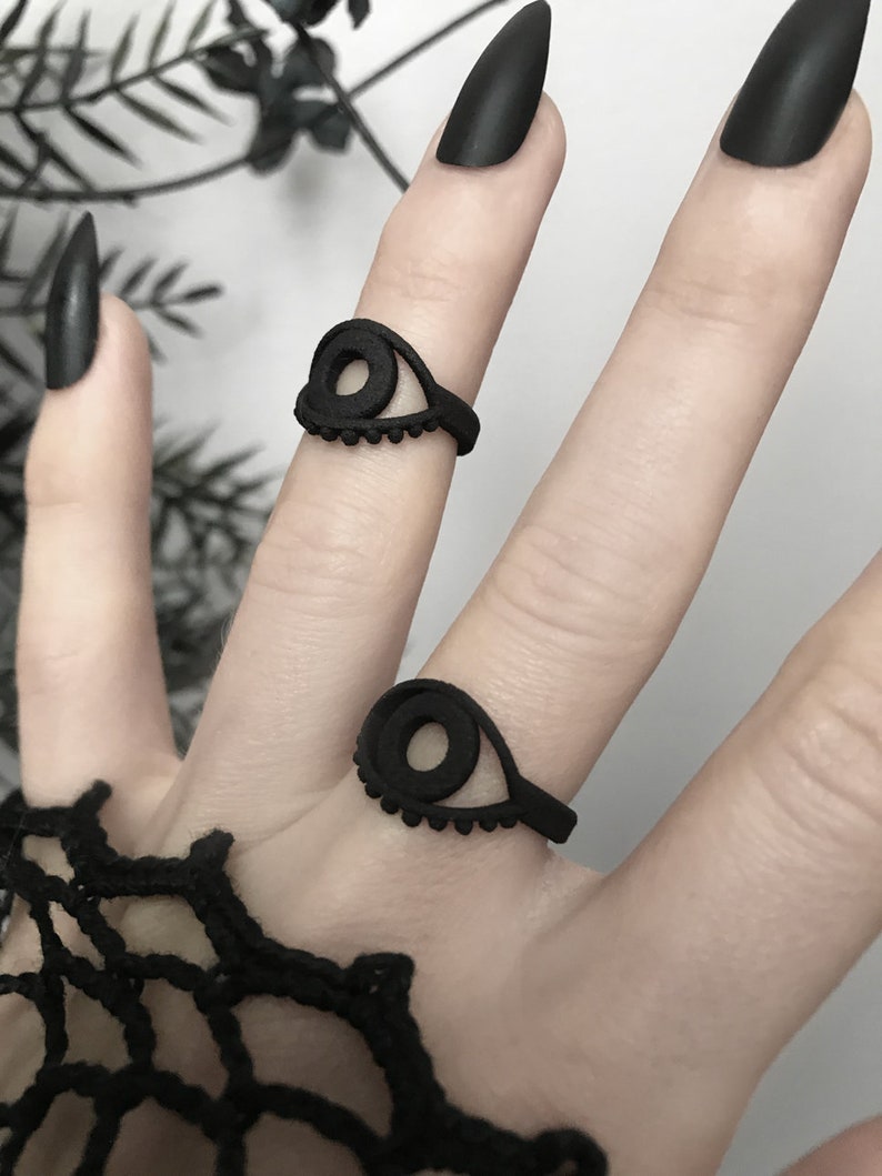 Matte black 3d printed eye ring displayed on a goth model hand with long black nails