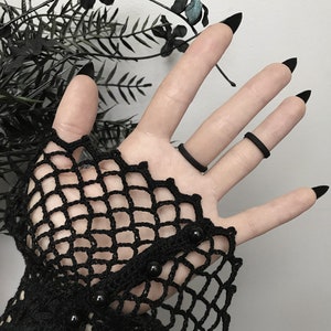 The plain side of a black 3d printed eye ring displayed on a gothic model hand with lace and long black nails