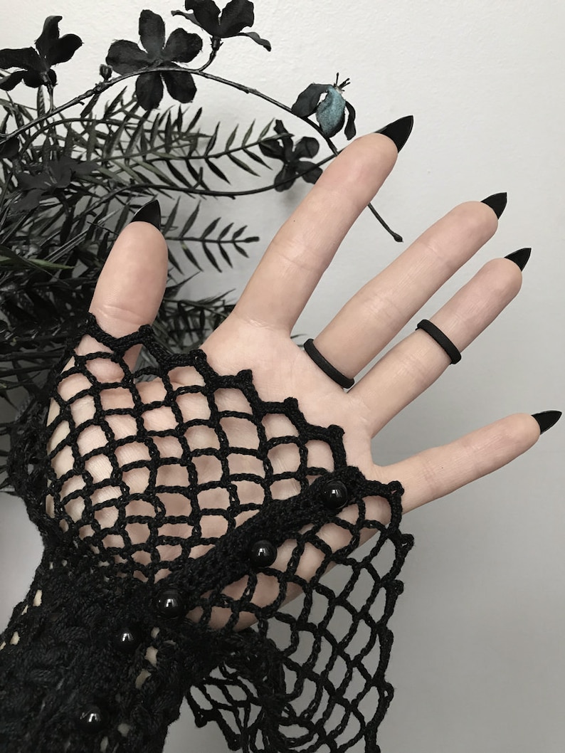 The plain side of a black 3d printed eye ring displayed on a gothic model hand with lace and long black nails