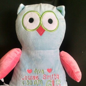 May include: A light blue plush owl with pink accents, featuring embroidered details. The owl has large eyes, a red beak, and pink wings and feet. Text on the owl includes a name, time, weight, and date. The owl is approximately 20 inches in height.