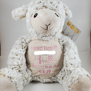 May include: A plush lamb toy with a cream-colored face and body, and a fluffy, textured exterior. The lamb has embroidered details and a cream-colored patch on its belly with the name "Scarlett Elizabeth", weight 7 pounds, 20 inches, 15 ounces, and the date 4.5.19.