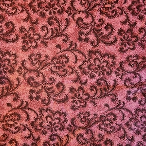 May include: Close-up of a textured fabric with a repeating floral pattern in shades of burgundy and pink. The design features stylized flowers and swirling vines, creating a vintage or Victorian aesthetic.