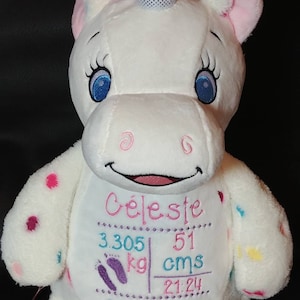 May include: A white plush unicorn with blue eyes, pink ears, and a silver horn. The unicorn has embroidered details, including the name "Celeste", weight 3.305 kg, height 51 cm, and birth date 04.02.13.