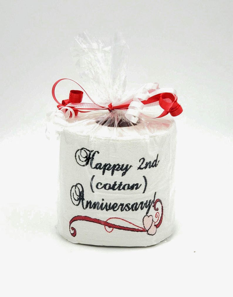 May include: A white toilet paper roll with a red ribbon and a black embroidered message that says "Happy 2nd (cotton) Anniversary" with two pink hearts.