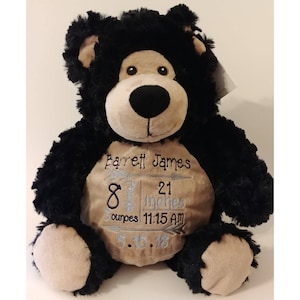 May include: A plush black bear with tan accents, featuring embroidered details. The bear has the name "Barrett James" and birth details: 8 pounds, 21 inches, 3 ounces, 11:15 AM, and 5.15.18.