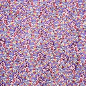 Puede incluir: Primer plano de una tela con un patrón de cachemira repetido. Las formas de cachemira son rojas y blancas, con un contorno morado. El fondo es de color morado claro con pequeños acentos florales amarillos y rosas.