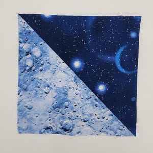 May include: Square fabric piece with a diagonal split design. One half depicts a detailed, light blue moon surface with craters. The other half shows a dark blue starry night sky with bright white stars and a crescent moon.