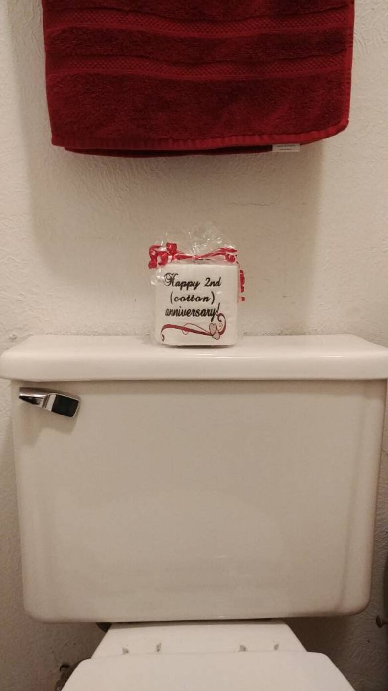 May include: A white toilet paper roll with a red ribbon and the text "Happy 2nd (cotton) anniversary!" on a white toilet tank.