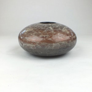 May include: A low, rounded ceramic vessel with a wide, flattened body and a small circular opening at the top. The surface features a glossy, multi-toned finish in shades of copper, brown, and gray, characterized by a distinct crackle pattern.