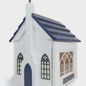 May include: A white wooden church-shaped box with a navy blue roof and cross. The box has arched windows and a door. The box is designed to hold books. The text "LittleChurchCorner" is visible on the side.