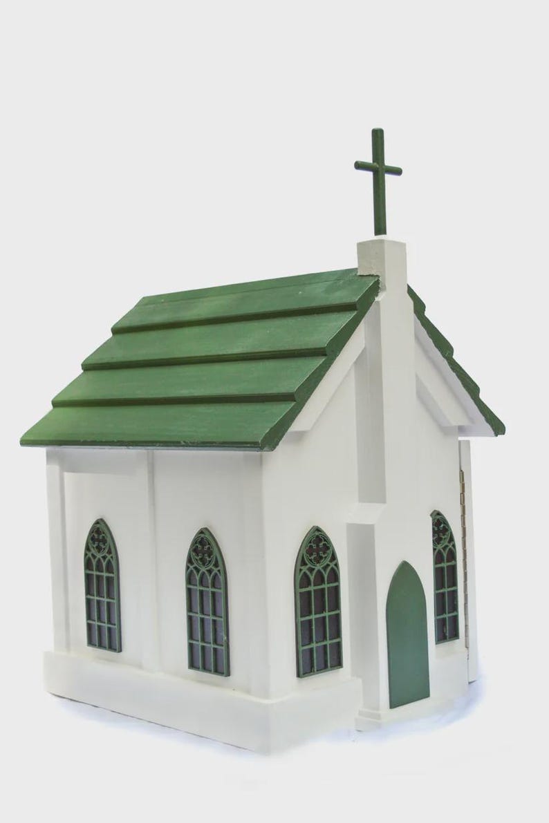 May include: A white wooden church model with a green roof and a cross on top. The church has arched windows with green trim and a green door. The model is a miniature replica of a church building.