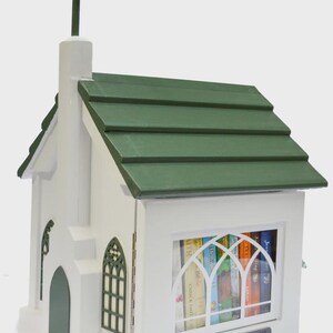 May include: A white wooden church-shaped Little Free Library with a green roof and cross. The library has a window with arched panes and contains books. The text "LittleChurchLibrary.org" is visible.