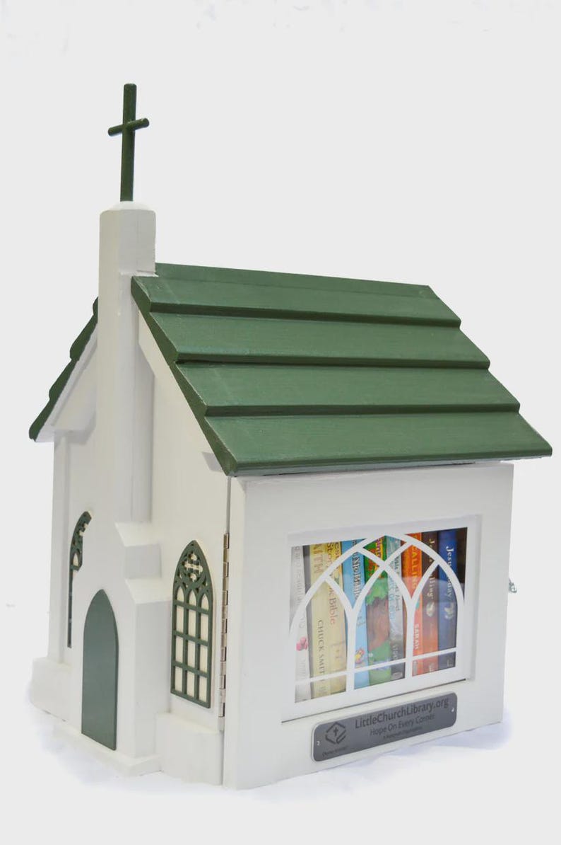 May include: A white wooden church-shaped Little Free Library with a green roof and cross. The library has a window with arched panes and contains books. The text "LittleChurchLibrary.org" is visible.