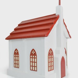 May include: A white wooden church model with a red roof and cross. The model features arched windows with a red trim and a red door. The roof is made of red wooden shingles.