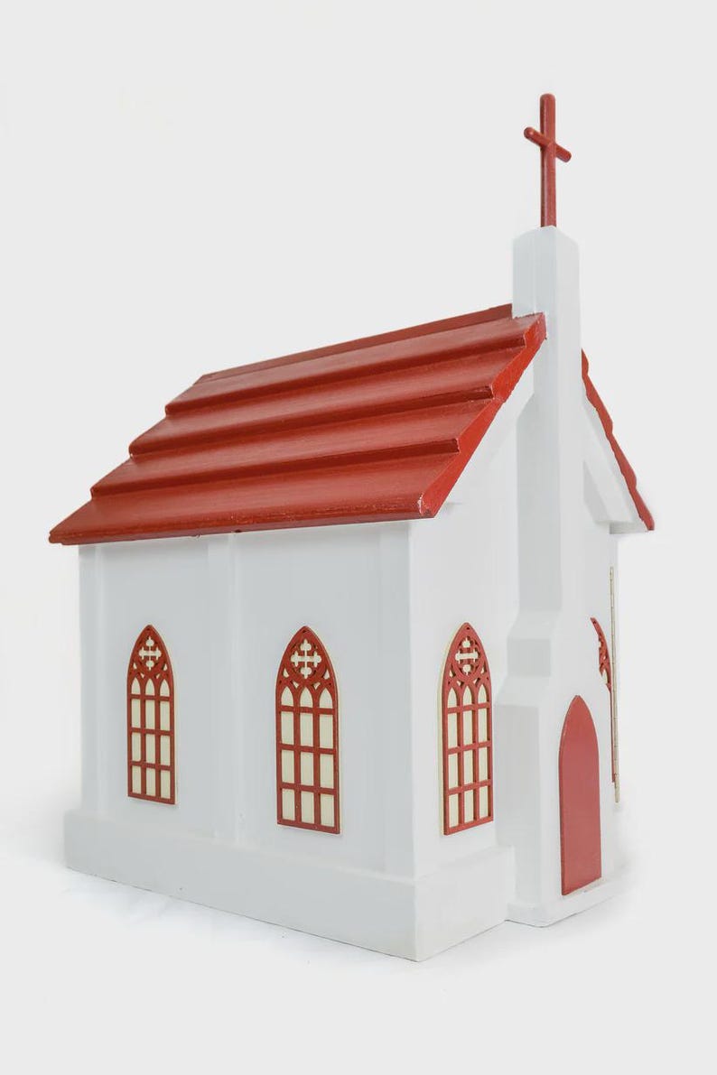 May include: A white wooden church model with a red roof and cross. The model features arched windows with a red trim and a red door. The roof is made of red wooden shingles.
