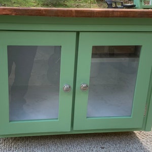 May include: A green wooden cabinet with two glass doors and silver knobs. The cabinet has a copper top.