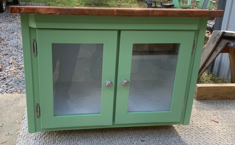 May include: A green wooden cabinet with two glass doors and silver knobs. The cabinet has a copper top.