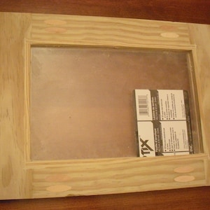 May include: A wooden frame with a clear glass insert. The frame has a light wood finish and is made of pine. The glass is clear and has a slight tint. The frame is 12 inches wide and 16 inches tall. The frame is sitting on a wooden surface.