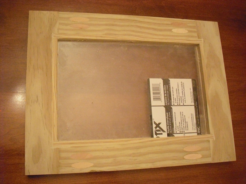 May include: A wooden frame with a clear glass insert. The frame has a light wood finish and is made of pine. The glass is clear and has a slight tint. The frame is 12 inches wide and 16 inches tall. The frame is sitting on a wooden surface.