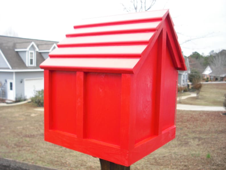 May include: A bright red wooden birdhouse with a gabled roof and a simple design. The birdhouse is mounted on a wooden post.
