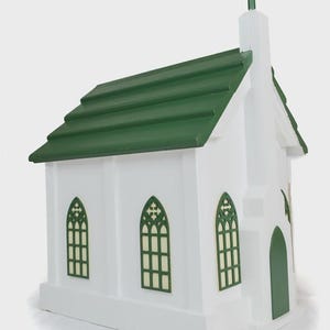 May include: A white miniature church with a green roof and cross. The building has three arched windows with green trim and a green door. The church is a decorative item.